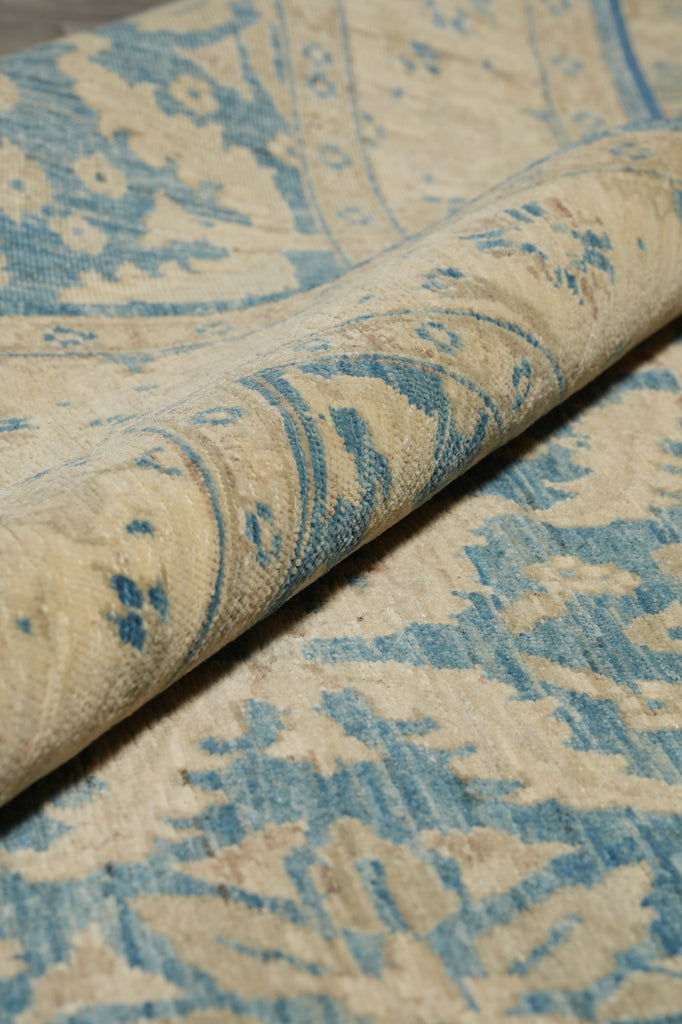 A close-up of a folded area rug showing its woven texture and a distressed blue and beige floral pattern.