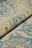 Load image into Gallery viewer, A close-up of a folded area rug showing its woven texture and a distressed blue and beige floral pattern.
