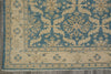 Load image into Gallery viewer, A close-up of a traditional patterned rug corner, showing a blue and beige floral design with a decorative border on a gray floor.