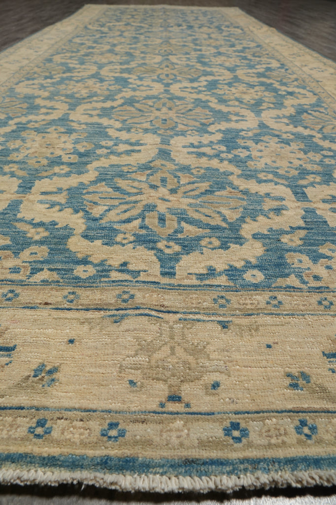 A close-up view of a traditional patterned area rug with a beige base and blue motifs, showing the woven texture and fringe detail.