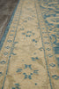 Load image into Gallery viewer, A close-up view of a traditional area rug with a beige base and blue distressed patterns, laid out on a gray tiled floor.