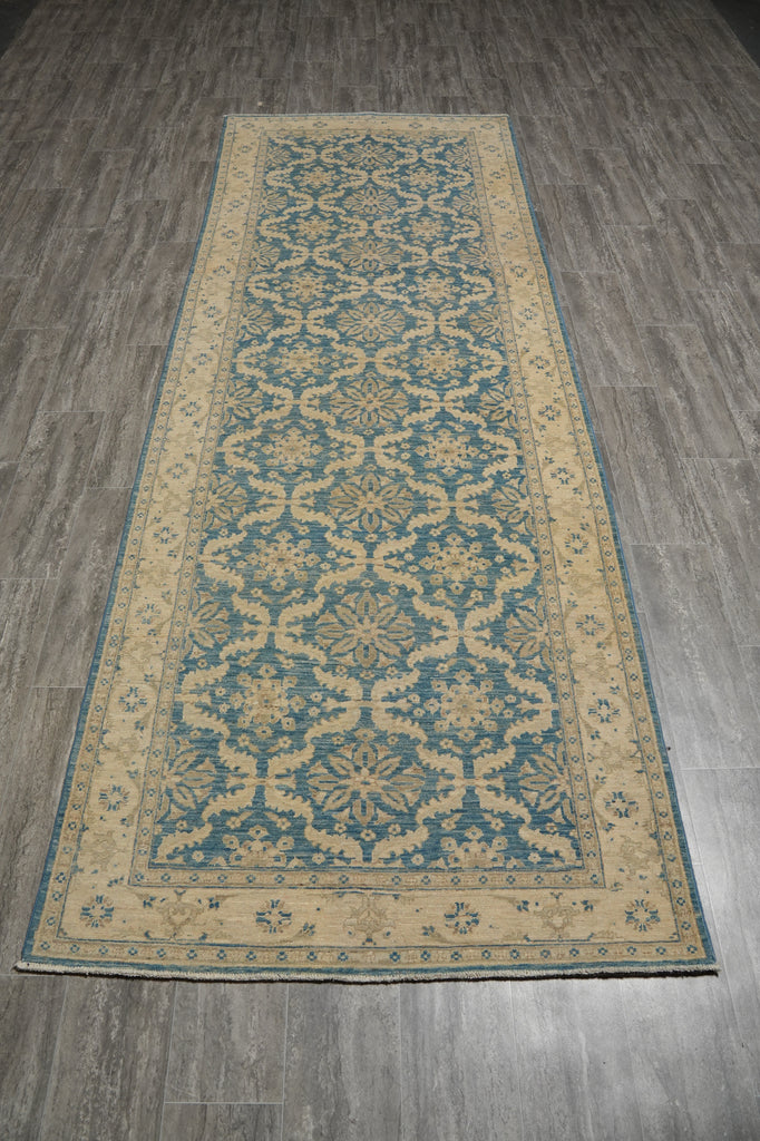 A long rectangular area rug with a traditional floral and geometric pattern in muted blue and beige, laid out on a gray wood-look floor.