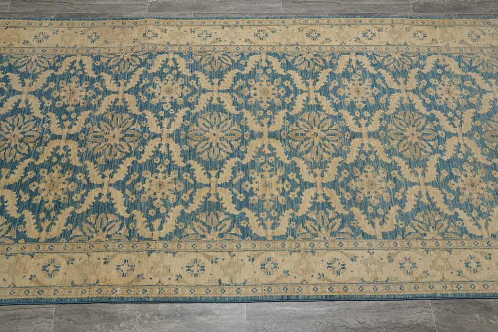 A rectangular area rug with a traditional ikat-style pattern in teal blue and beige, laid flat on a gray tiled floor.