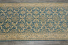 Load image into Gallery viewer, A rectangular area rug with a traditional ikat-style pattern in teal blue and beige, laid flat on a gray tiled floor.