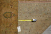 Load image into Gallery viewer, A square area rug with an ornate traditional floral pattern in beige, brown, and muted green tones, shown with a yellow tape measure and a price tag laid across it on a neutral surface.