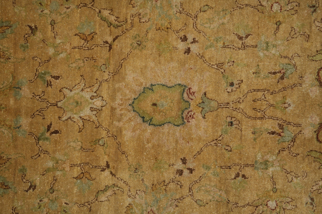 A close-up of an antique-style area rug with a distressed floral pattern in warm tan, beige, muted green, and brown tones.