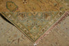 Load image into Gallery viewer, A close-up of a traditional patterned rug corner with fringe, showing a muted sage green border and floral motifs in beige, tan, and dusty pink tones over a warm brown field.