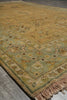 Load image into Gallery viewer, A traditional oriental-style area rug with a warm mustard yellow center and a sage green border, laid out on a gray tiled floor.