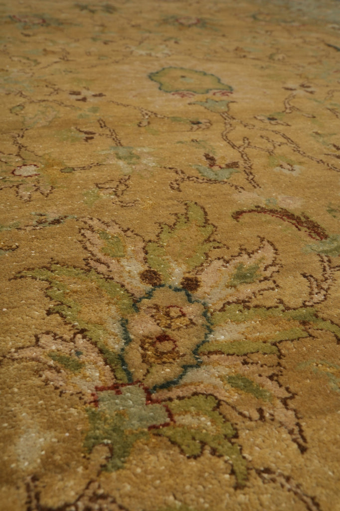 A close-up view of a traditional area rug with a floral motif in warm beige, muted green, and brown tones.