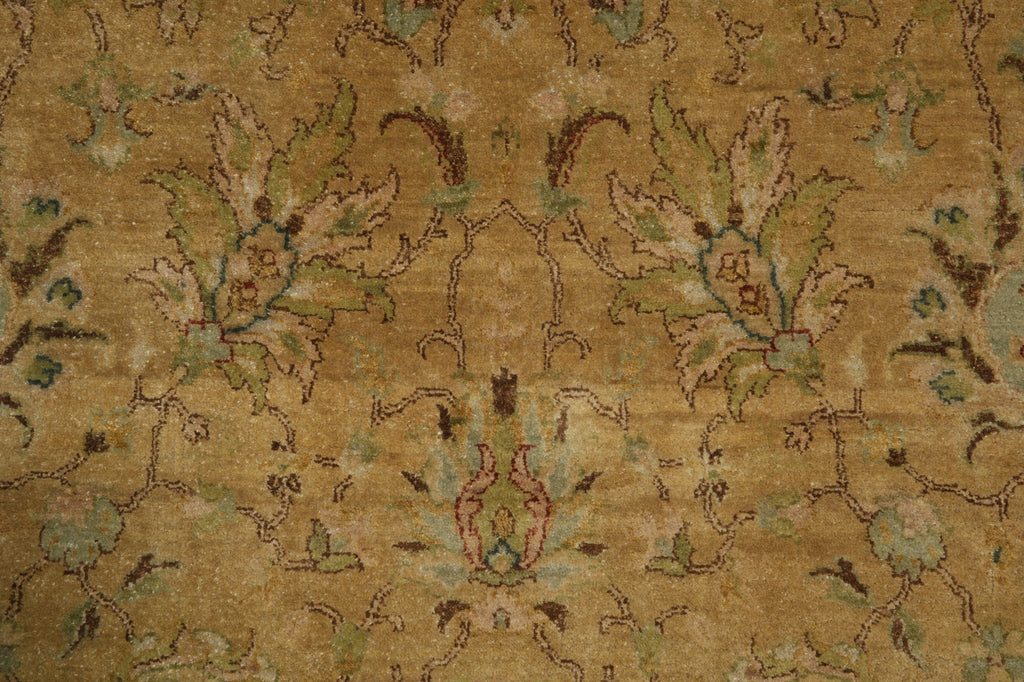 A close-up of a traditional patterned rug with a warm tan and beige background, featuring muted green, brown, and light blue floral motifs.