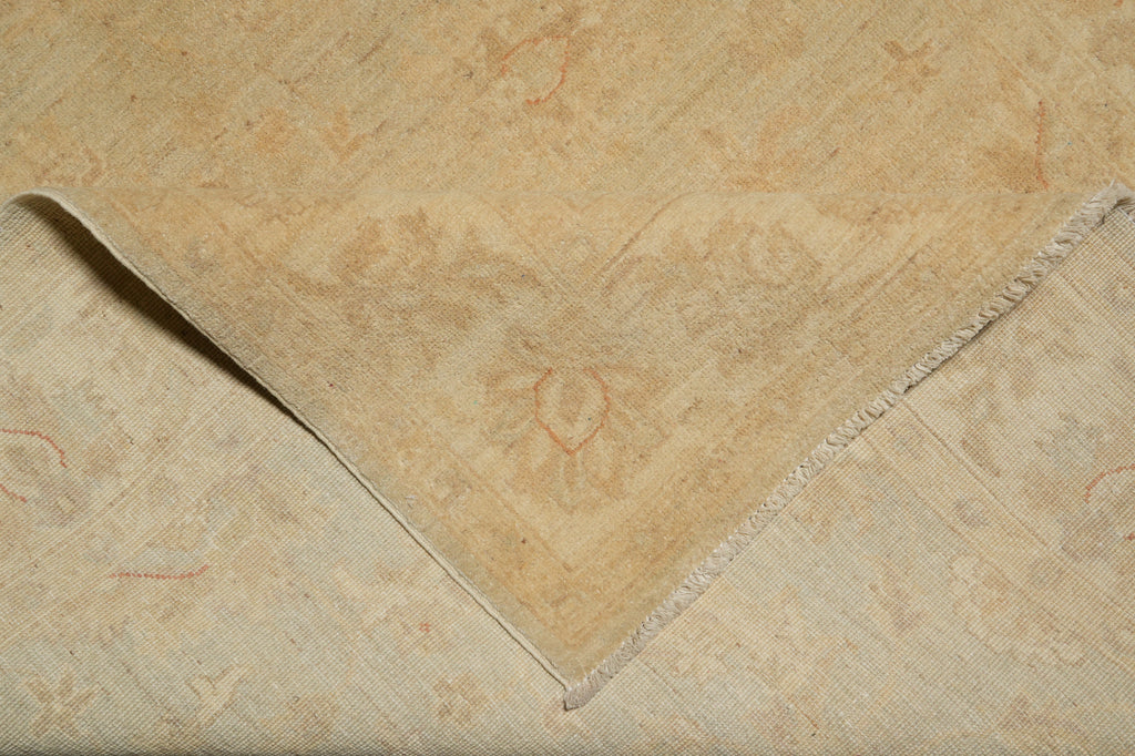 A close-up of a folded beige area rug with a subtle, faded traditional floral pattern and fringed edges.