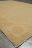 Load image into Gallery viewer, A close-up of a light beige area rug with subtle faded floral patterns and fringed edges, laid out on a gray floor.