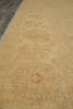 Load image into Gallery viewer, A close-up view of a beige area rug with a subtle, faded traditional pattern and a small red accent near the bottom center.