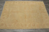 Load image into Gallery viewer, A large rectangular area rug in a warm sandy beige color with a subtle faded traditional floral pattern, laid flat on a dark gray tiled floor.