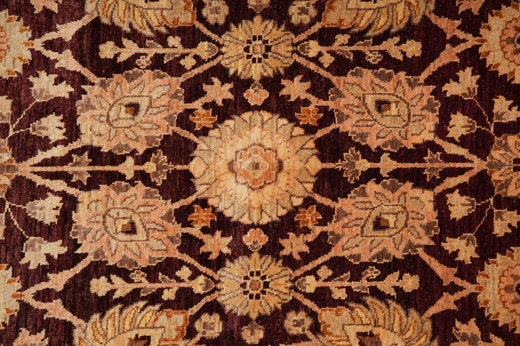 A close-up of an ornate traditional rug featuring a symmetrical floral and medallion pattern in warm beige, tan, and rust tones over a very dark brown to near-black background.