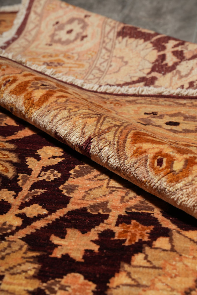 A close-up of a folded area rug showing its intricate traditional pattern in warm tones of beige, brown, and deep burgundy.