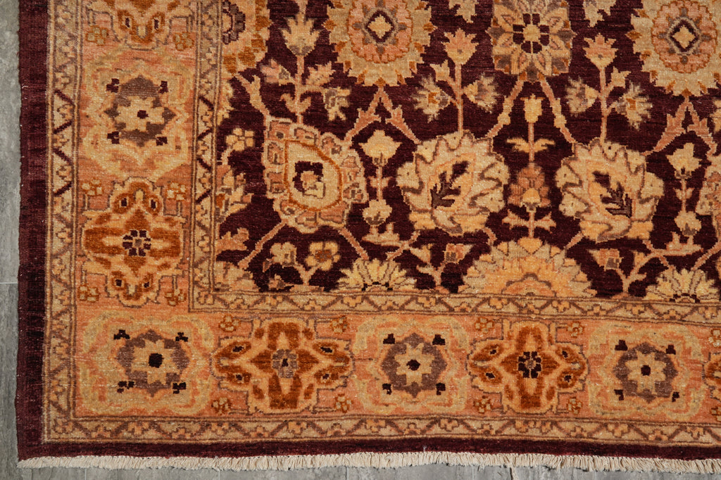 A close-up of an ornate patterned rug corner showing a dark burgundy field with beige floral motifs and a warm rust-orange border.