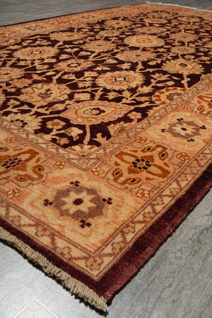 An ornate traditional area rug with a complex floral and geometric pattern in shades of dark brown, rust orange, and beige, shown laid out on a gray tiled floor.