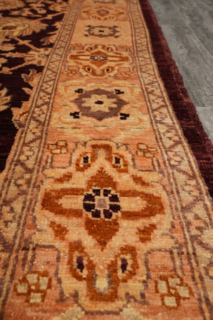 A close-up view of a traditional oriental rug with a warm rust-orange, beige, and brown geometric pattern, laid out on a gray floor.