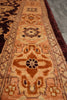 Load image into Gallery viewer, A close-up view of a traditional oriental rug with a warm rust-orange, beige, and brown geometric pattern, laid out on a gray floor.