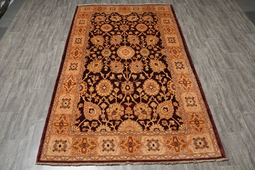 A rectangular traditional area rug with an intricate floral and medallion pattern, laid flat on a gray wood-look floor. The rug features a dark brown center, a warm tan and orange inner border, and a deep red outer border.