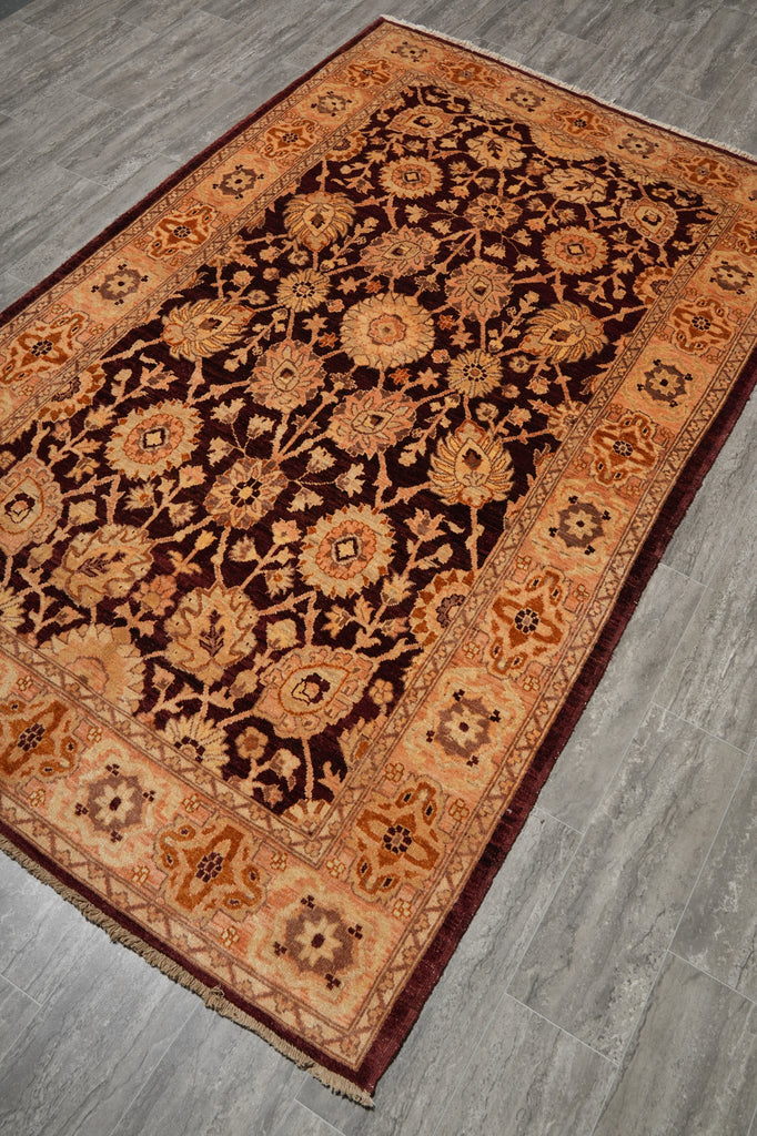 An oriental-style area rug with an intricate floral pattern, shown laid out on a gray wood-look floor. The rug features a dark brown center field with beige and orange floral motifs, surrounded by a warm tan border with red accents.