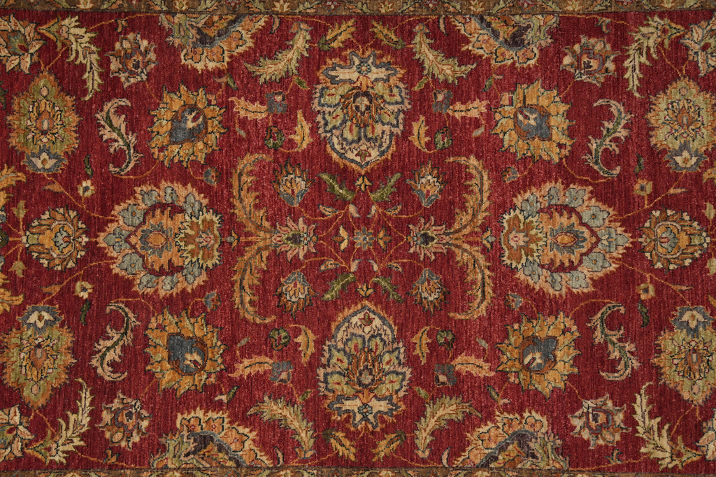 A close-up of an ornate traditional rug with a deep red field and intricate floral motifs in beige, blue, and muted green.