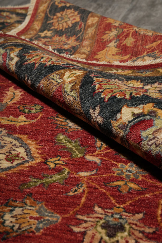 A close-up of a folded traditional area rug showing its detailed floral pattern in red, beige, black, and muted green tones.