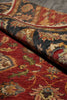 Load image into Gallery viewer, A close-up of a folded traditional area rug showing its detailed floral pattern in red, beige, black, and muted green tones.
