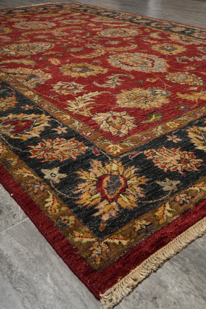 A traditional oriental area rug with a deep red field, black borders, and beige floral motifs, shown laid out on a gray tiled floor.