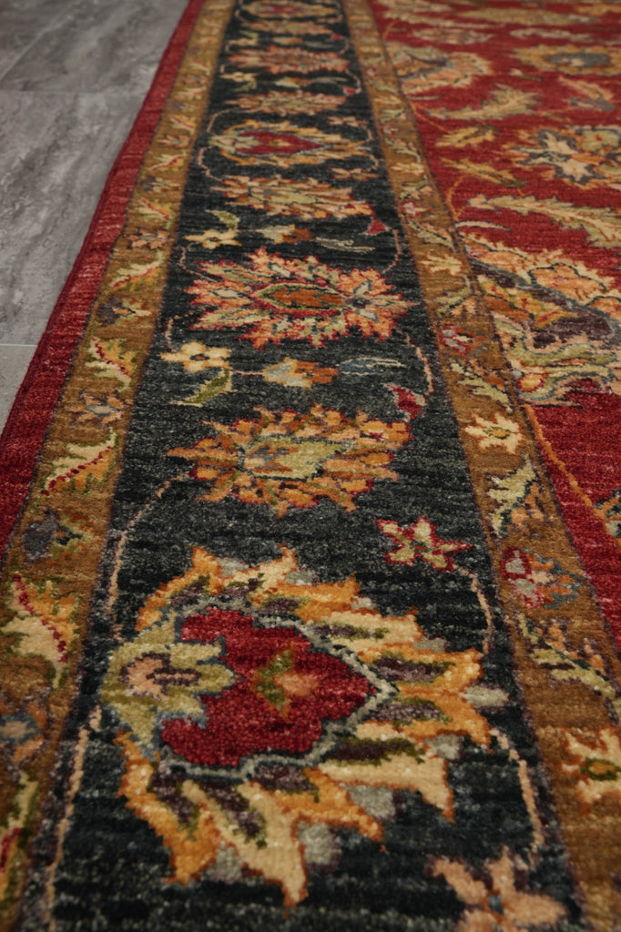 A close-up view of an ornate area rug with a dark charcoal central field, red borders, and floral motifs in beige, rust, and gold tones.