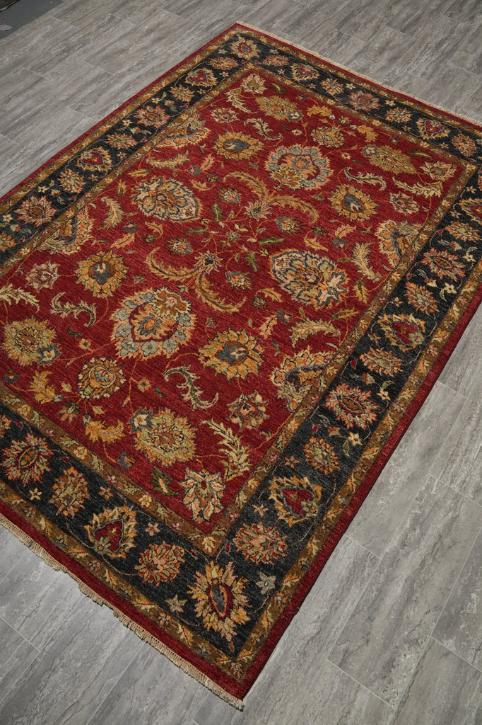 A traditional oriental area rug with a deep red field, ornate floral motifs, and dark borders, shown laid out on a gray wood-look floor.