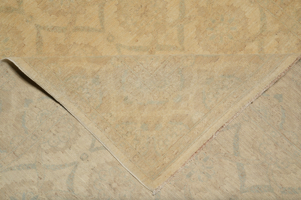 A close-up of a beige area rug with a faded traditional pattern, showing a folded corner that reveals the underside and frayed edges.