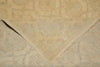 Load image into Gallery viewer, A close-up of a beige area rug with a faded traditional pattern, showing a folded corner that reveals the underside and frayed edges.