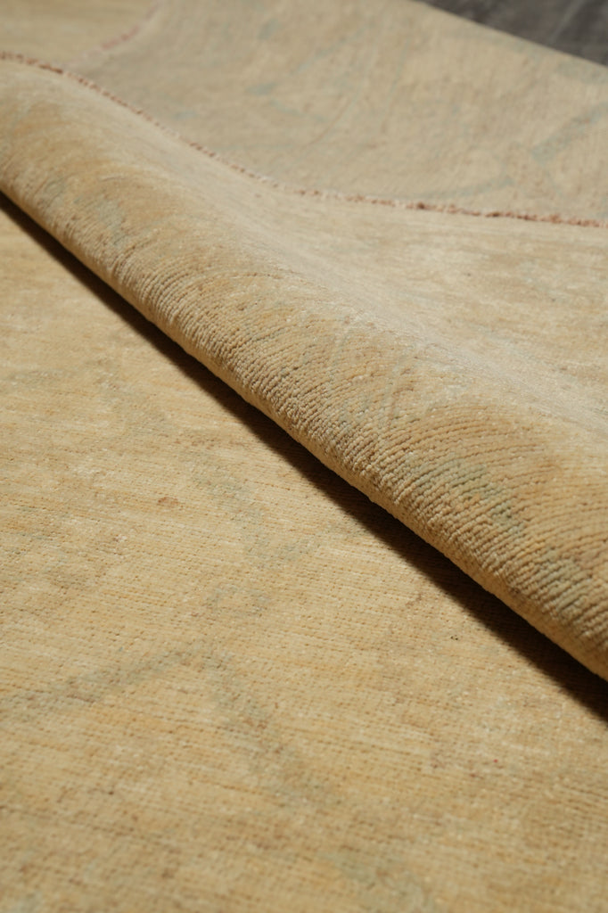 Close-up of a beige woven rug with a rolled corner showing the texture and pile, on a neutral surface.