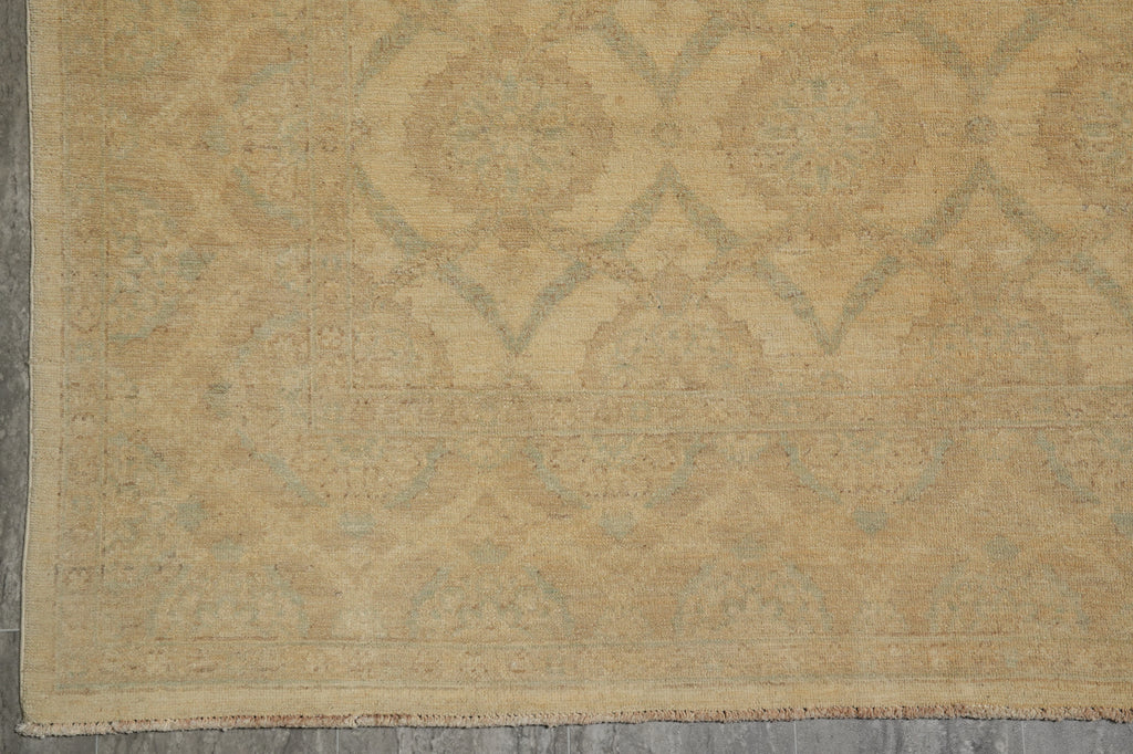 A close-up of a beige area rug with a faded traditional medallion pattern in muted gray-green tones, showing the woven texture and fringe edge.