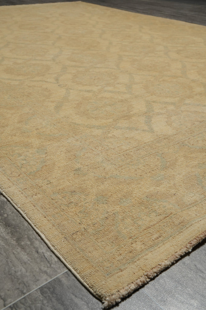 A close-up view of a beige area rug with a subtle distressed medallion pattern, shown on a gray tiled floor.