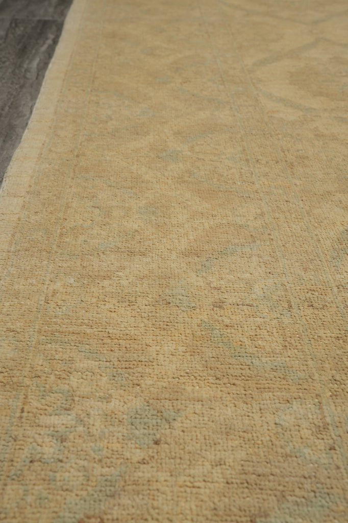 A close-up view of a textured area rug in warm beige with a subtle light blue-gray distressed pattern, shown on a dark wood floor.