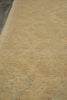 Load image into Gallery viewer, A close-up view of a textured area rug in warm beige with a subtle light blue-gray distressed pattern, shown on a dark wood floor.