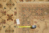 Load image into Gallery viewer, A close-up of a patterned area rug in beige, brown, and muted red tones, shown with a yellow tape measure and a small white tag on a matching rug surface.
