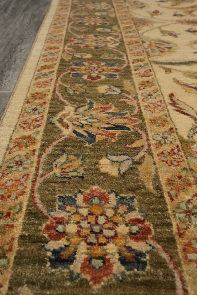 A close-up view of a traditional oriental area rug with a floral medallion pattern in olive green, beige, rust red, and navy blue.