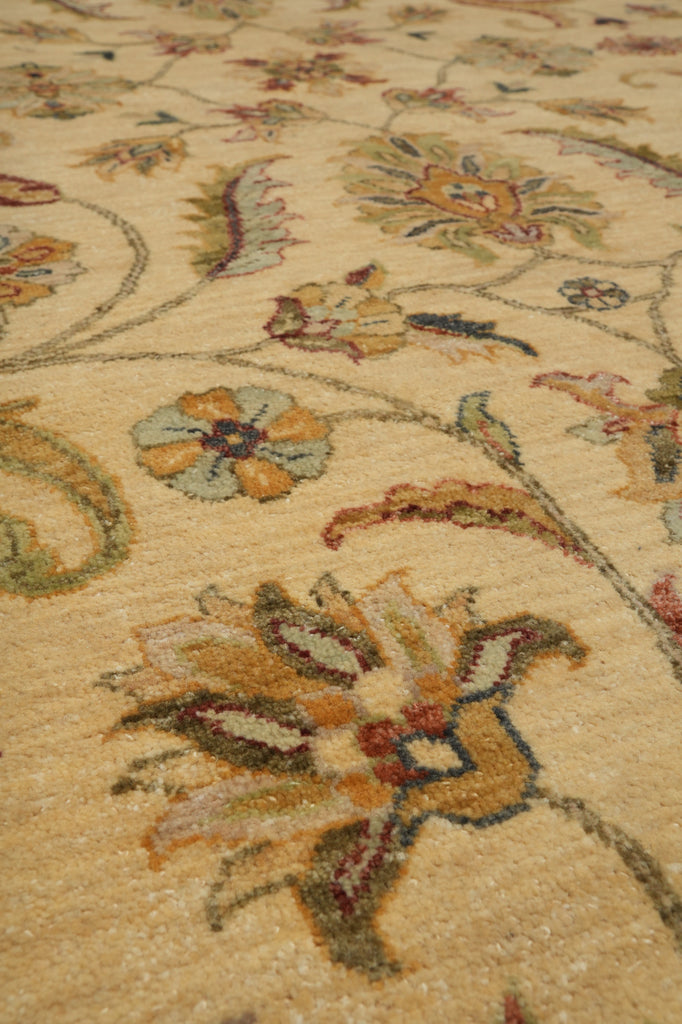 Close-up of a traditional floral area rug with a warm beige background and multicolored embroidered or woven floral motifs in muted orange, green, blue, and brown tones.