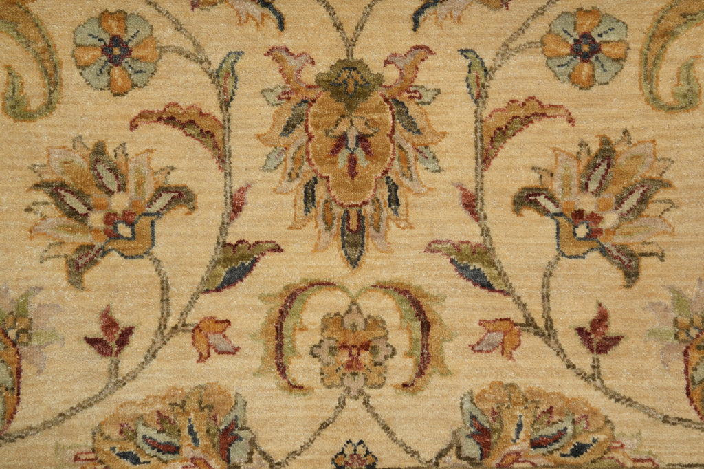 Close-up of a woven floral rug pattern on a warm beige background, featuring cream, tan, muted green, and brown botanical motifs.