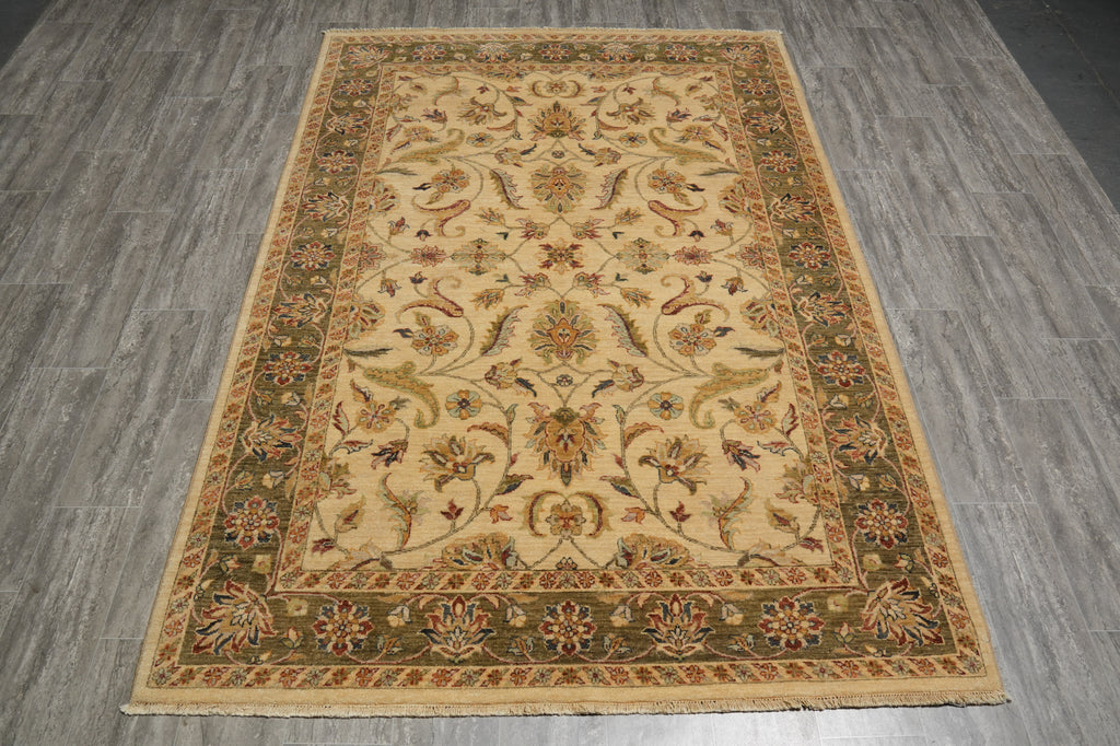 A rectangular traditional area rug with an ornate floral and vine pattern, laid out on a gray wood-look floor. The rug features a beige center field surrounded by olive green and rust-brown borders.