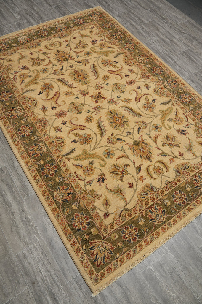 An oriental area rug with a beige center and a dark green border, featuring intricate floral and vine patterns in muted red, brown, and gold tones, laid out on a gray wood-look floor.