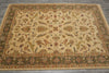 Load image into Gallery viewer, An oriental-style area rug with an intricate floral and vine pattern, featuring a beige center field, green borders, and accents of orange, red, and blue, laid out on a gray tiled floor.