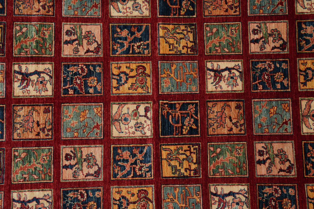 A close-up of a patterned textile or rug featuring a grid of small square panels with traditional motifs in beige, blue, green, and gold, separated by a deep red border.