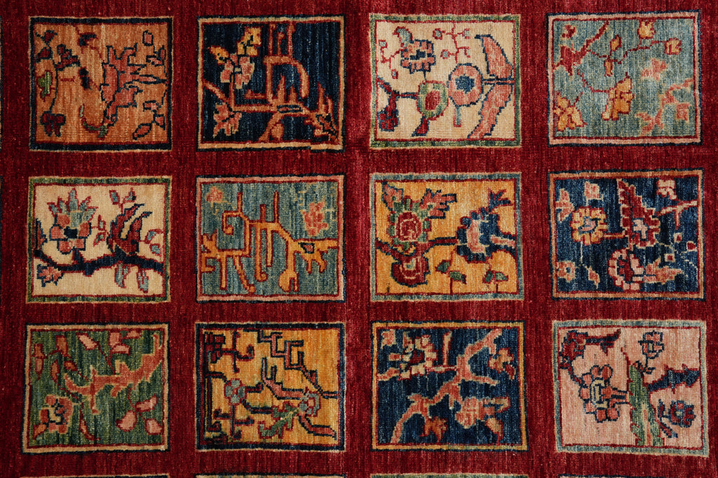 A close-up of a woven rug or textile featuring a grid of 12 square panels with abstract floral and geometric motifs in navy, mustard, beige, and green, set against a deep red field.