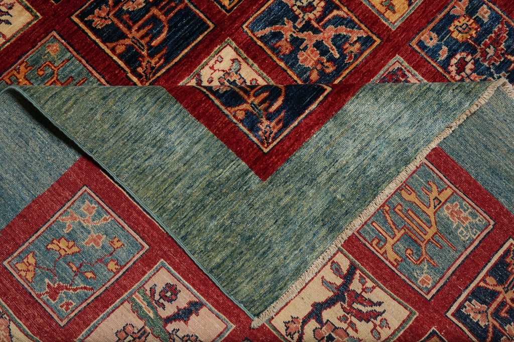 A close-up of a patterned area rug showing both the top and reverse sides. The top side features a geometric border with floral motifs in red, navy, and beige.