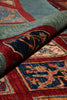 Load image into Gallery viewer, A close-up of a patterned area rug with a rolled section showing its underside. The rug features a deep red border, a blue central field, and a sage green outer section with traditional geometric and floral motifs in beige and blue.